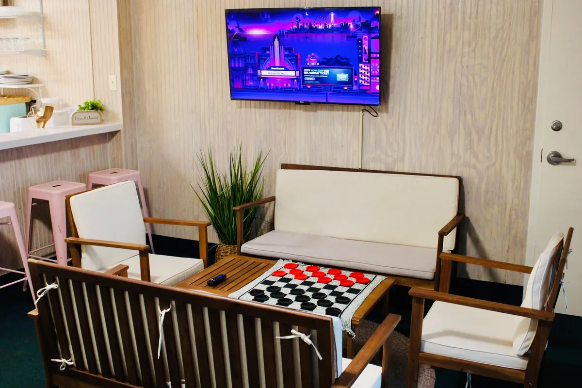 The image showcases a welcoming studio interior featuring a comfy sofa, a stylish checkerboard table ideal for games or coffee, and a television—inviting guests to relax, socialize, or enjoy a movie night.