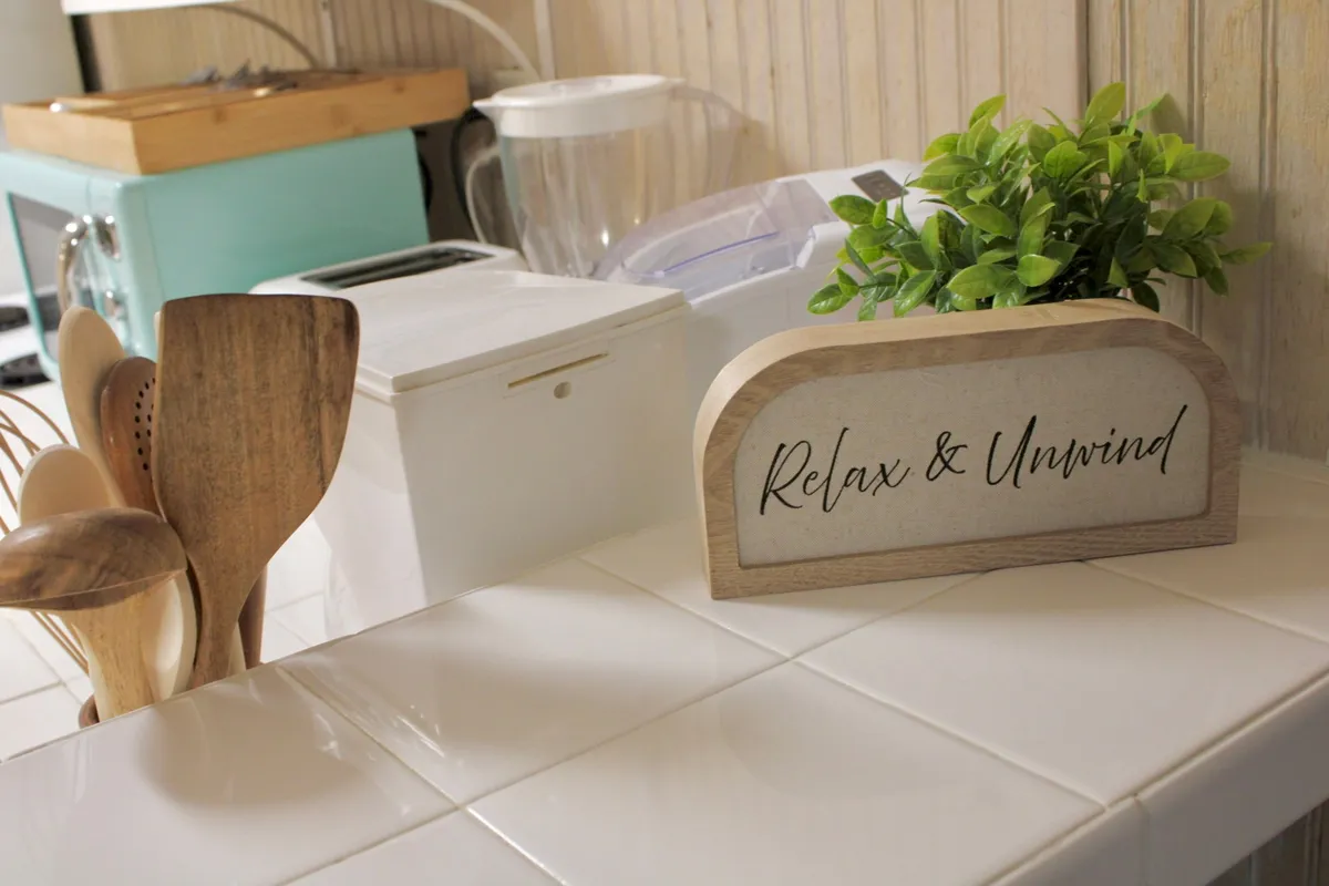 A cozy studio interior featuring a countertop with wooden utensils, a potted green plant, and a decorative sign. The setup suggests a homey, relaxed atmosphere that's comfortable for both guests and their pets.